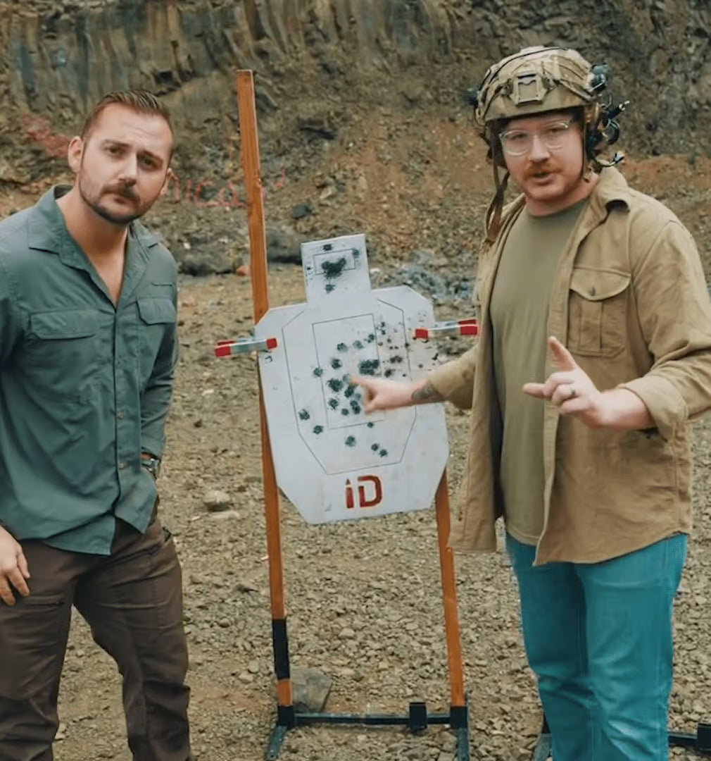Two men standing next to a target with bullet holes in an outdoor setting